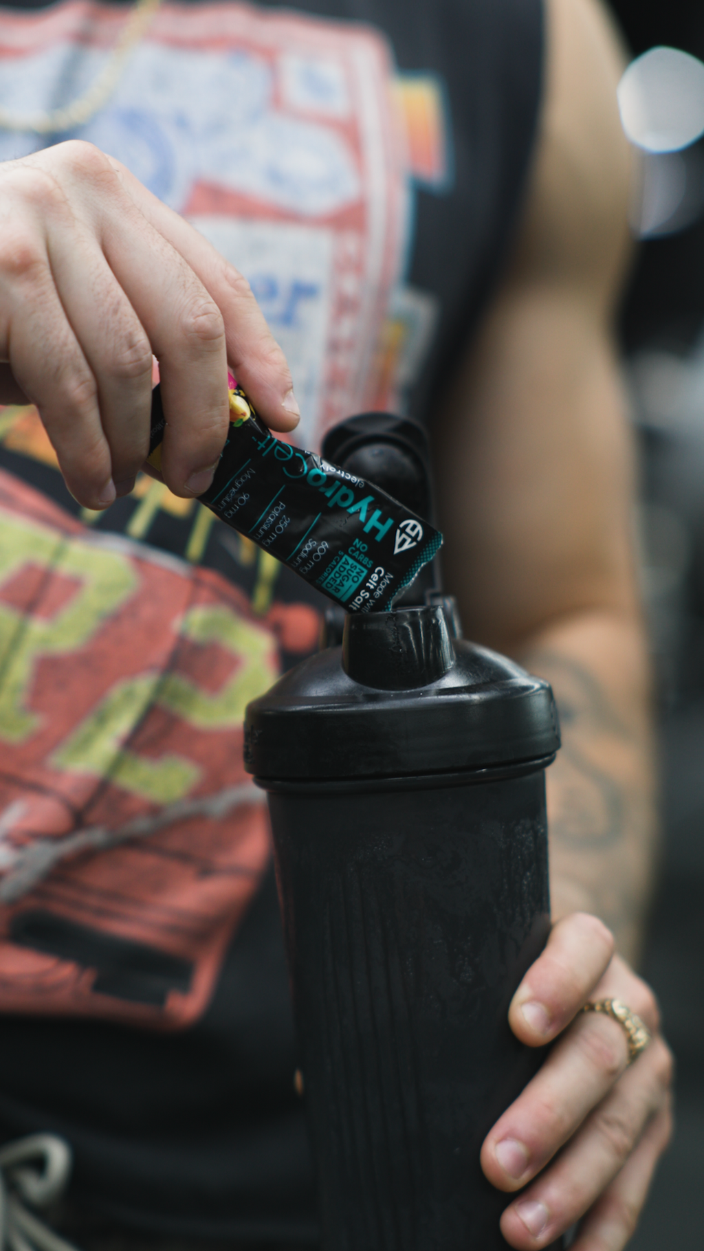 Person holding a black water bottle with a colorful shirt in the background