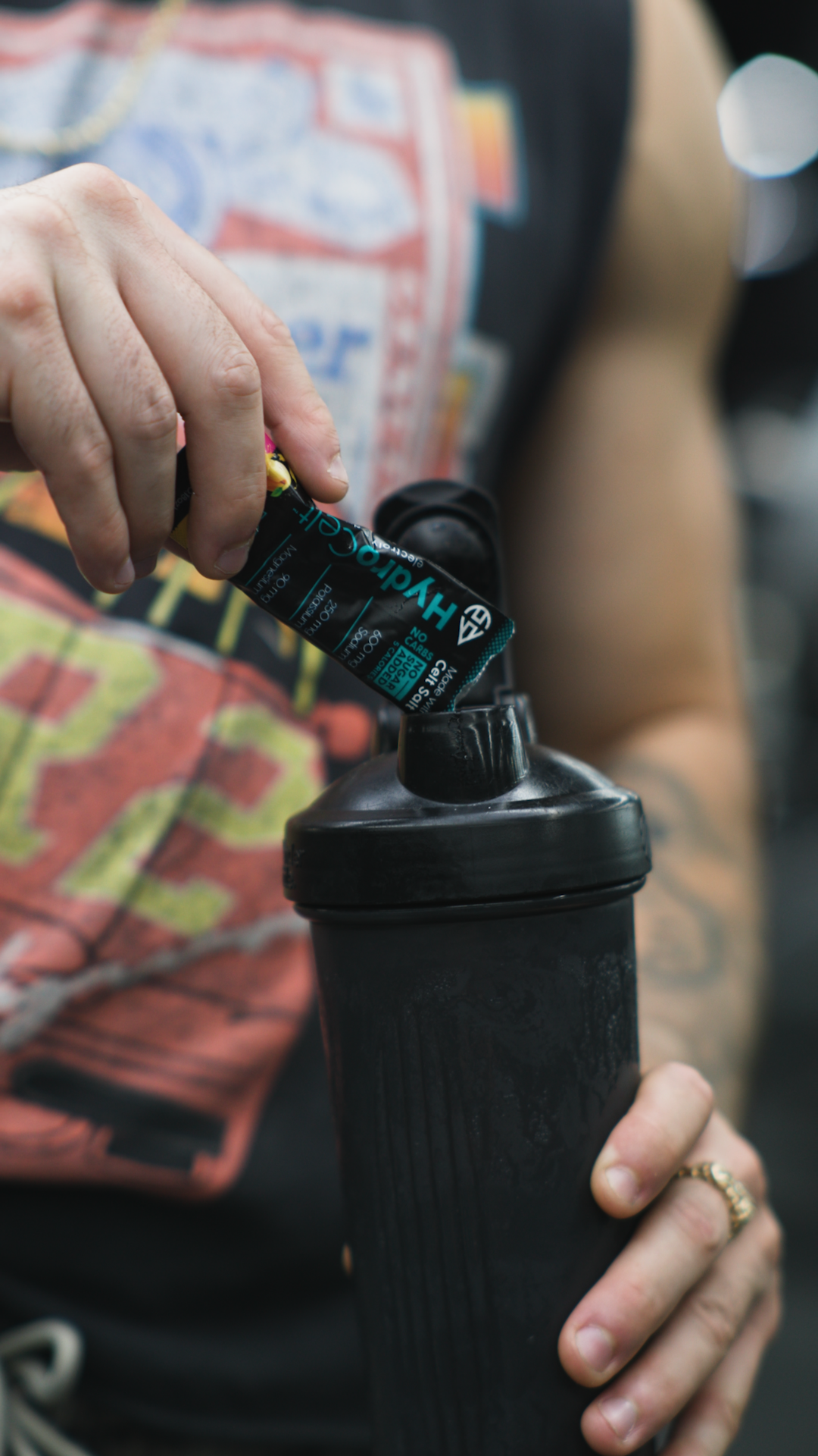 Person holding a black water bottle with a colorful shirt in the background